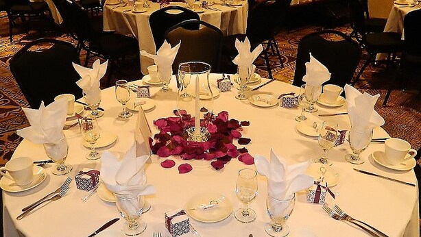 A round dining table set for a formal meal with white tablecloths, silverware, and glassware.