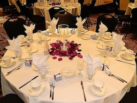 A round dining table set for a formal meal with white tablecloths, silverware, and glassware.