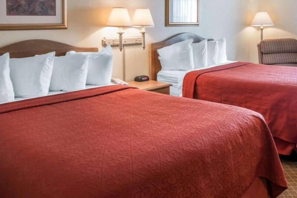 A hotel room with two beds, a nightstand, a lamp, and a framed picture on the wall.