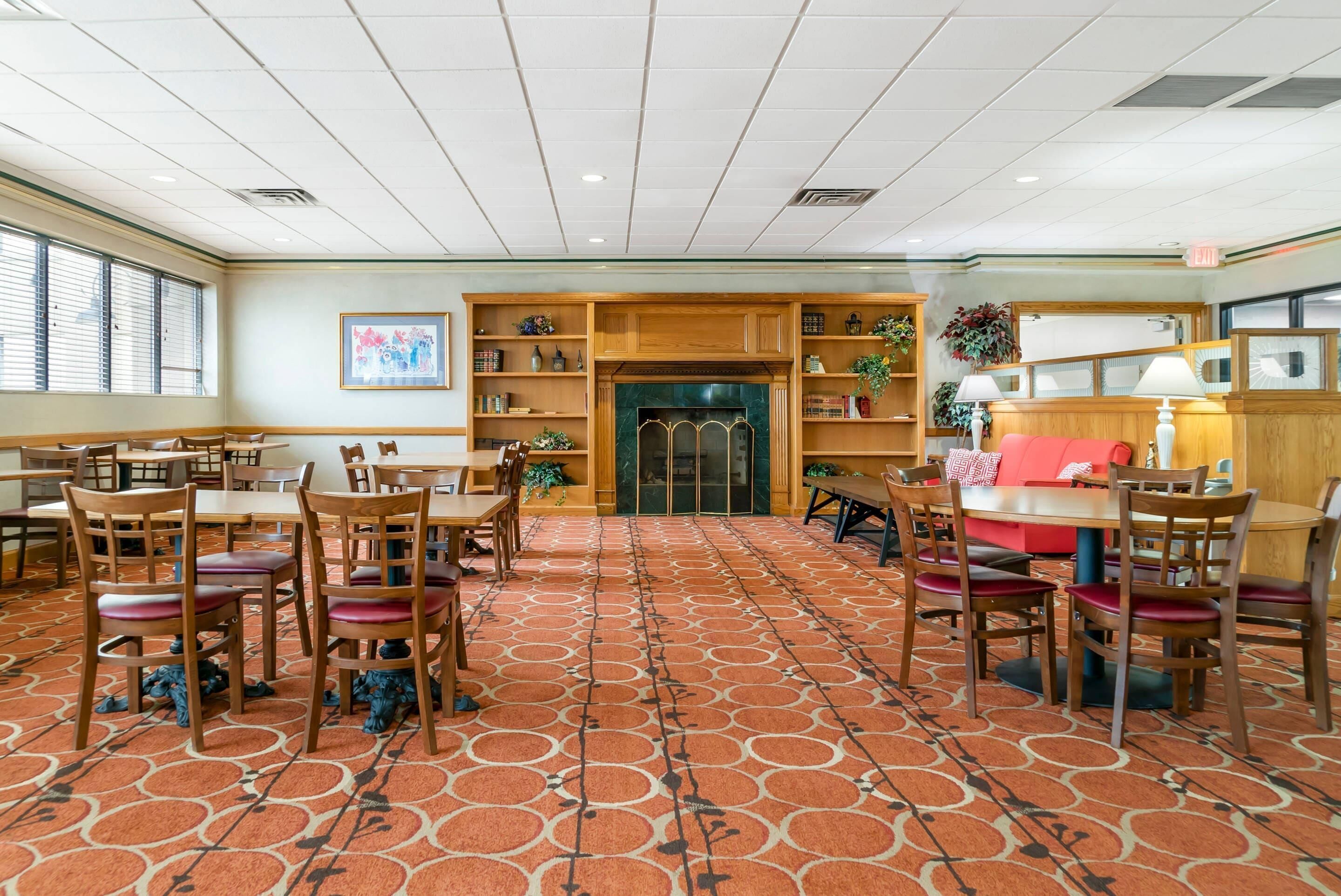 A hotel lobby with a patterned carpet, wooden furniture, and a fireplace.