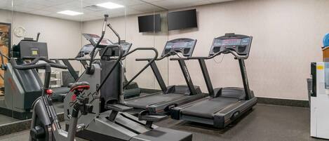 Un gimnasio con cintas de correr, elípticas y una bicicleta estática.