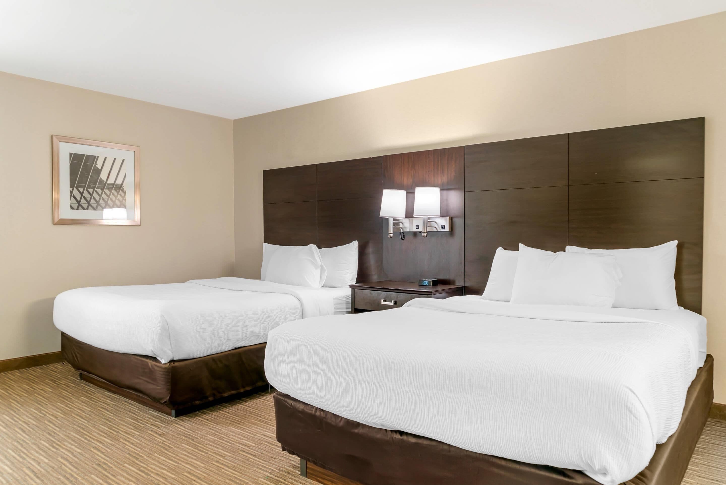 Habitación de hotel con dos camas, una mesita de noche y una lámpara en la pared.