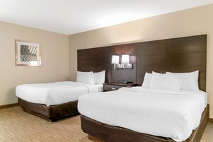 Habitación de hotel con dos camas, una mesita de noche y una lámpara en la pared.