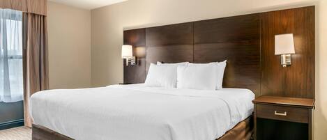 A hotel room with a large bed, two bedside lamps, a wooden headboard, and a nightstand with a drawer.