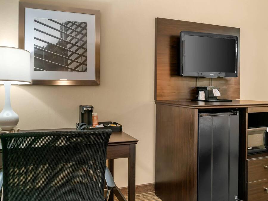 Hotelkamer met een bureau, stoel, lamp, flatscreen televisie, minibar en een ingelijst schilderij aan de muur.