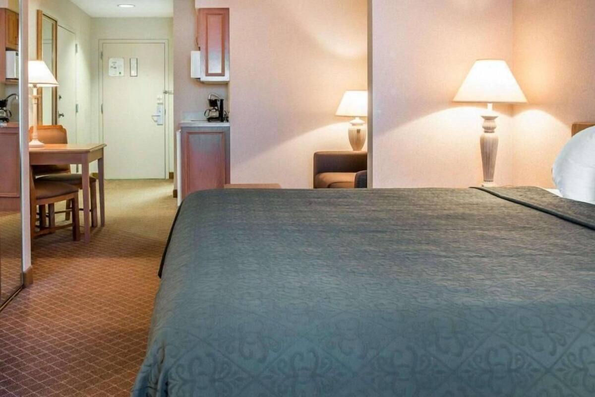 A hotel room with a bed, a desk, a chair, a lamp, and a wardrobe.