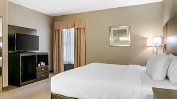 Habitación de hotel con cama, televisión sobre un mueble, escritorio con lámpara y ventana con cortinas.