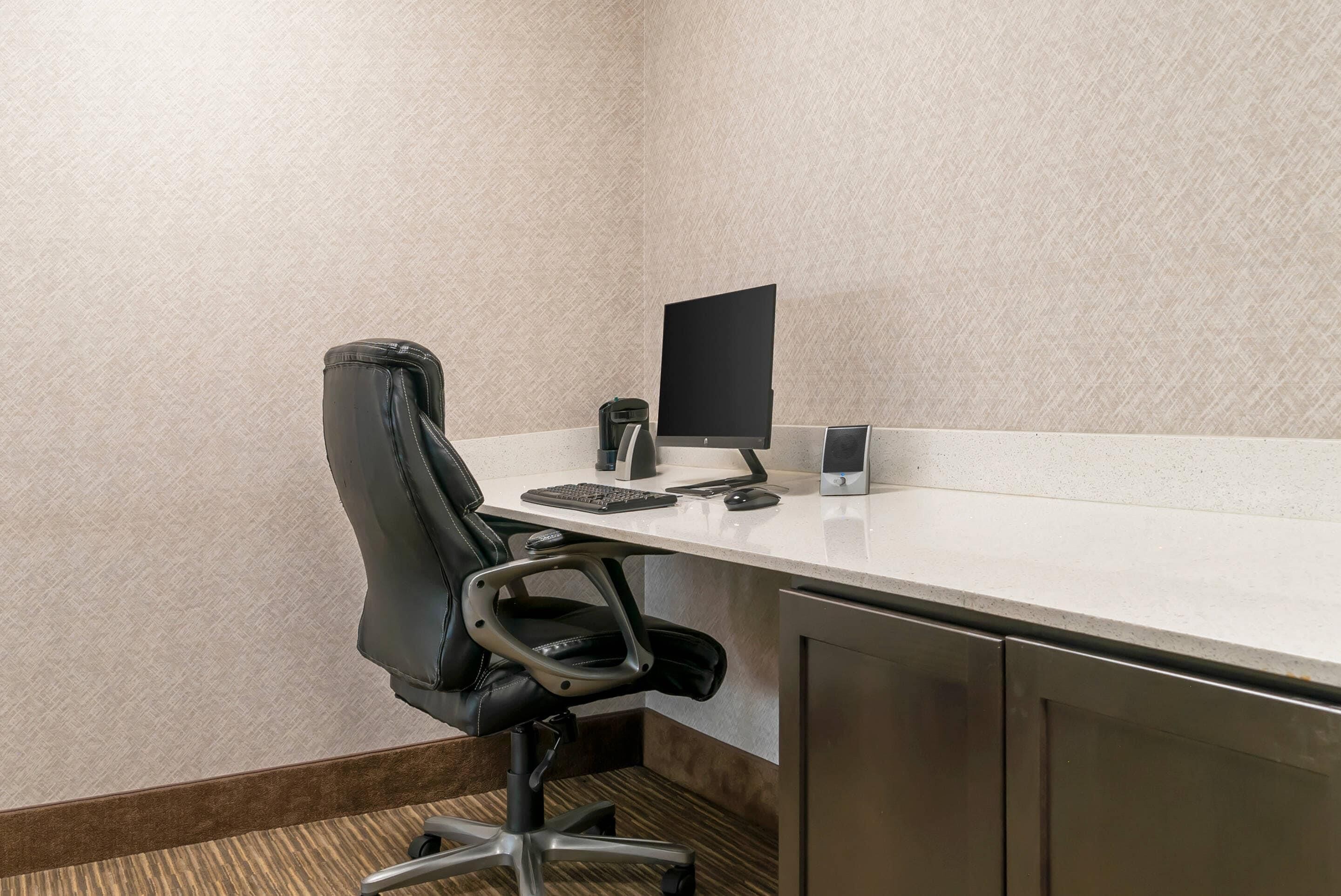A small office space with a desk, chair, computer, keyboard, mouse, and a small trash bin.