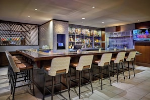 A bar area with a long counter, bar stools, and a television screen.