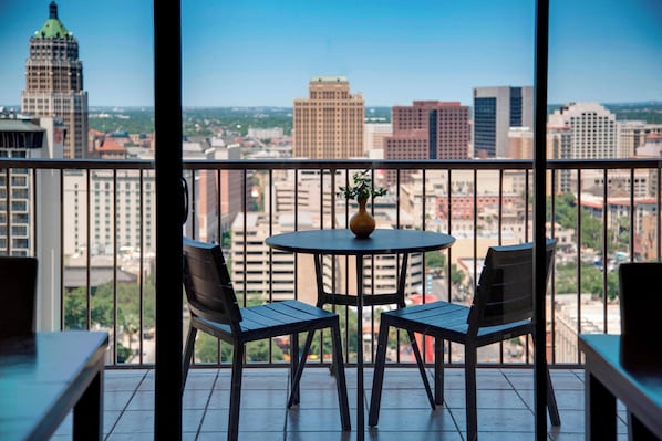 A balcony with two chairs and a table, overlooking a cityscape with various buildings.