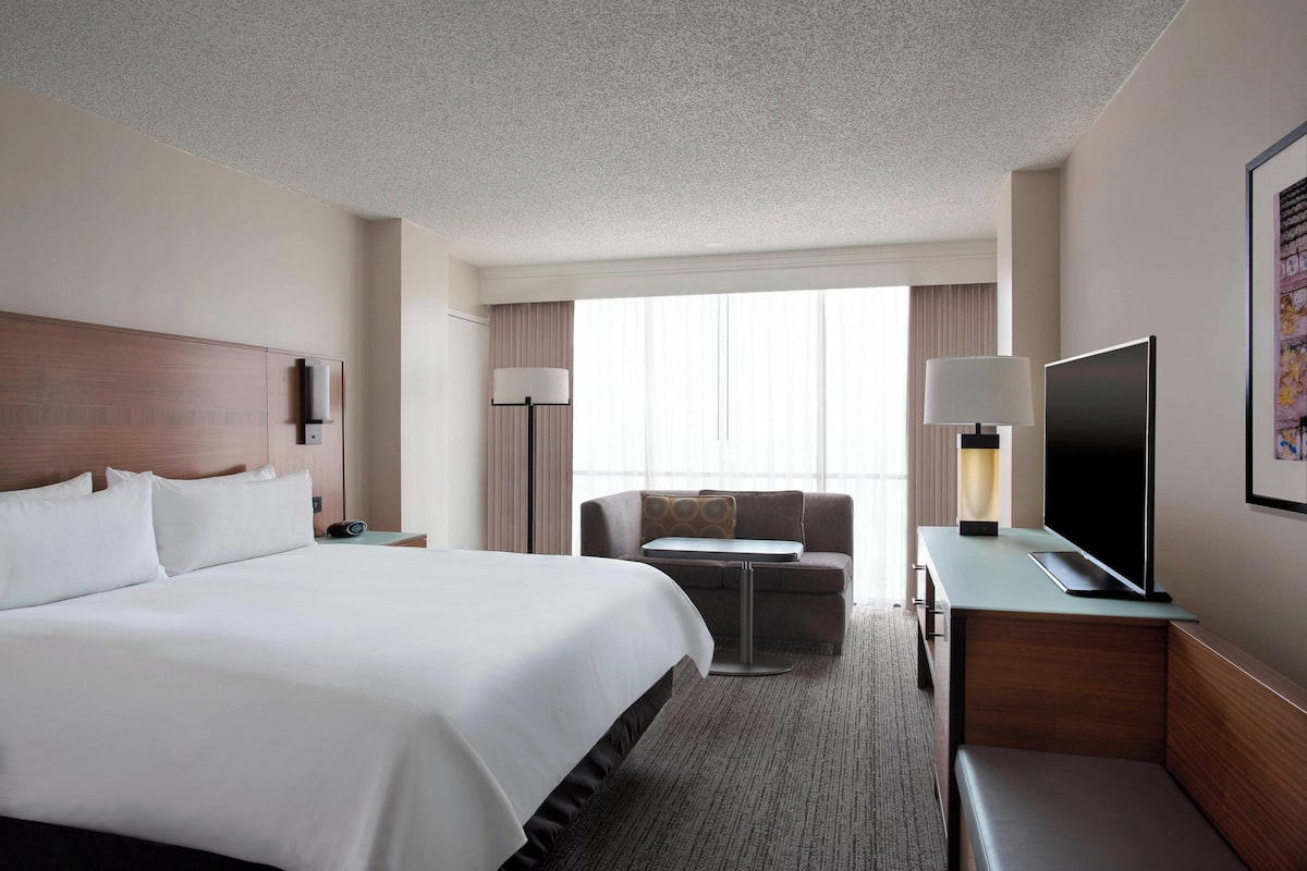 Une chambre d’hôtel avec un grand lit, un bureau doté d’un téléviseur à écran plat, un canapé et une grande fenêtre avec des rideaux.