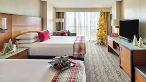 Habitación de hotel con dos camas, un televisor, un árbol de Navidad y una mesita con una bandeja de aperitivos.