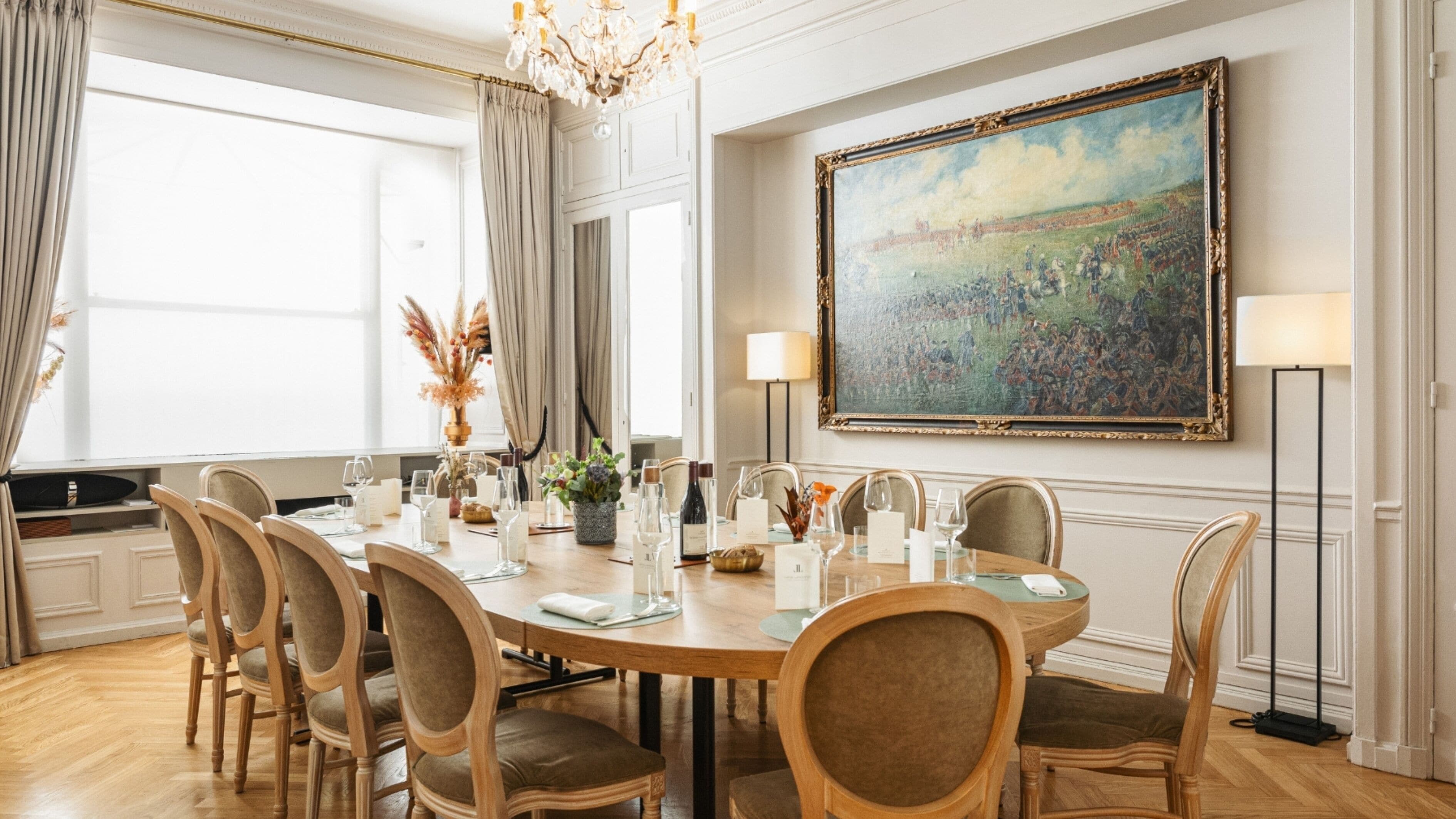 Une salle à manger élégante, avec une grande table dressée pour un repas, entourée de chaises, et un grand tableau accroché au mur.