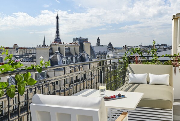 A rooftop terrace with a view of the Eiffel Tower, a table with a glass of water, and a sofa with cushions. - Hotel Lancaster (Paris)