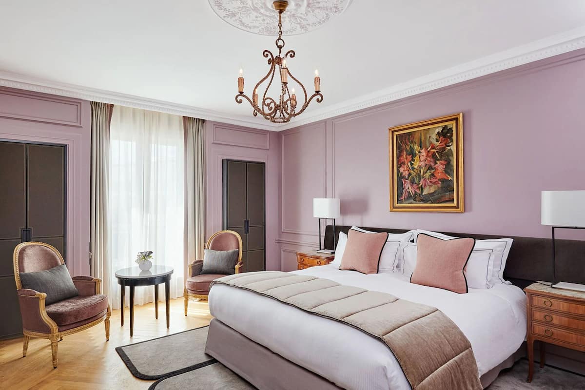 Un dormitorio con una cama grande, dos sillas, una mesita, un candelabro y un cuadro en la pared.