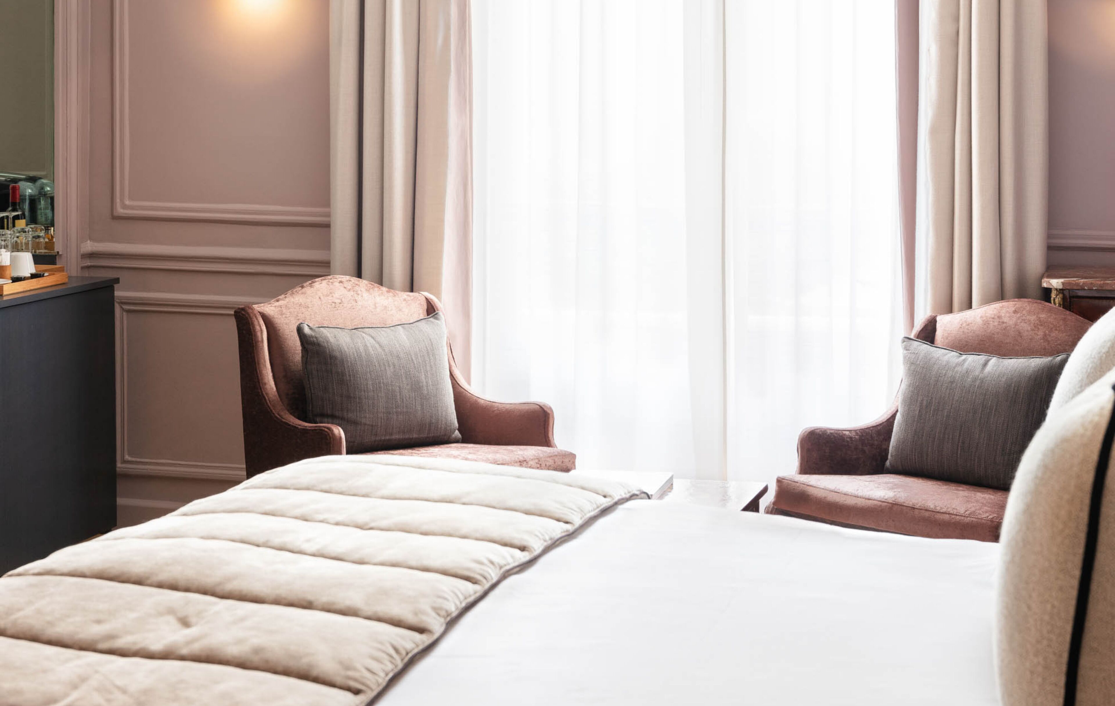 A hotel room with two armchairs, a bed, a nightstand, and a dresser.