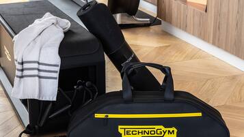 A home gym setup with exercise equipment, a yoga mat, and a towel on a wooden floor.