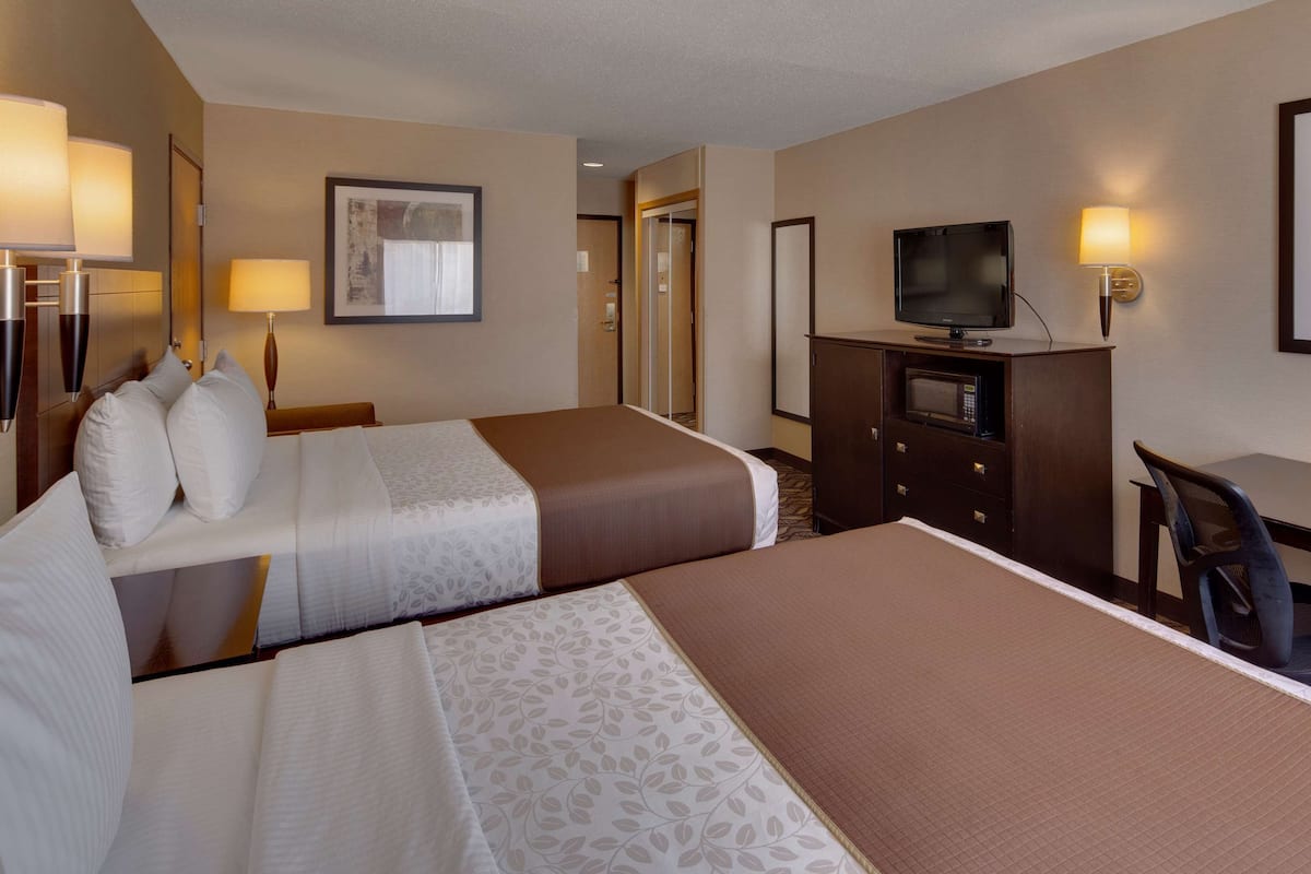 A hotel room with two beds, a desk, a television, and a framed picture on the wall.