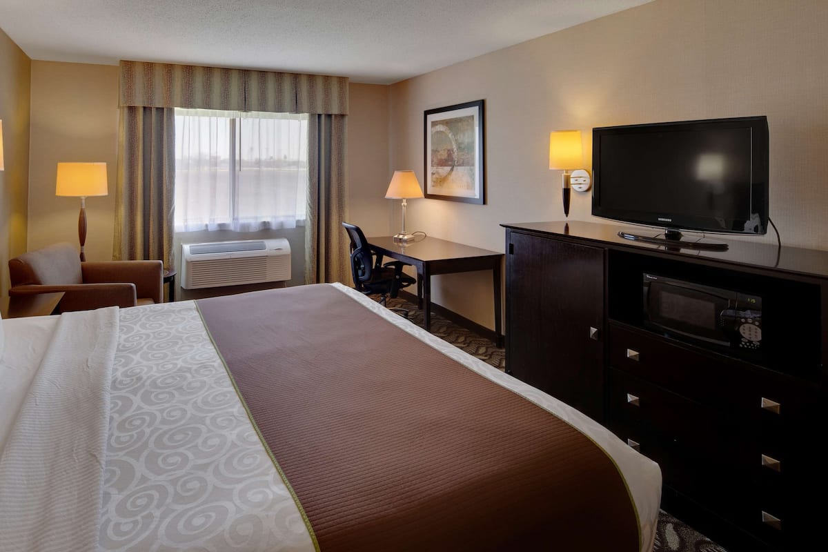 A hotel room with a large bed, a desk, a television, and an air conditioning unit.