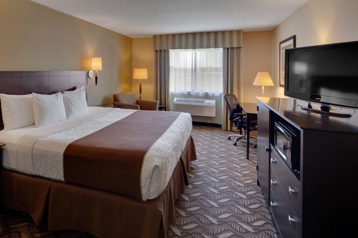 A hotel room with a large bed, bedside lamps, a television, a desk, and an air conditioning unit.