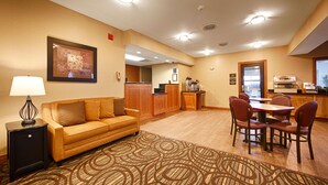 A hotel room with a sofa, a dining table with chairs, a kitchen area, and a patterned rug. - Best Western Pontiac Inn (Pontiac)