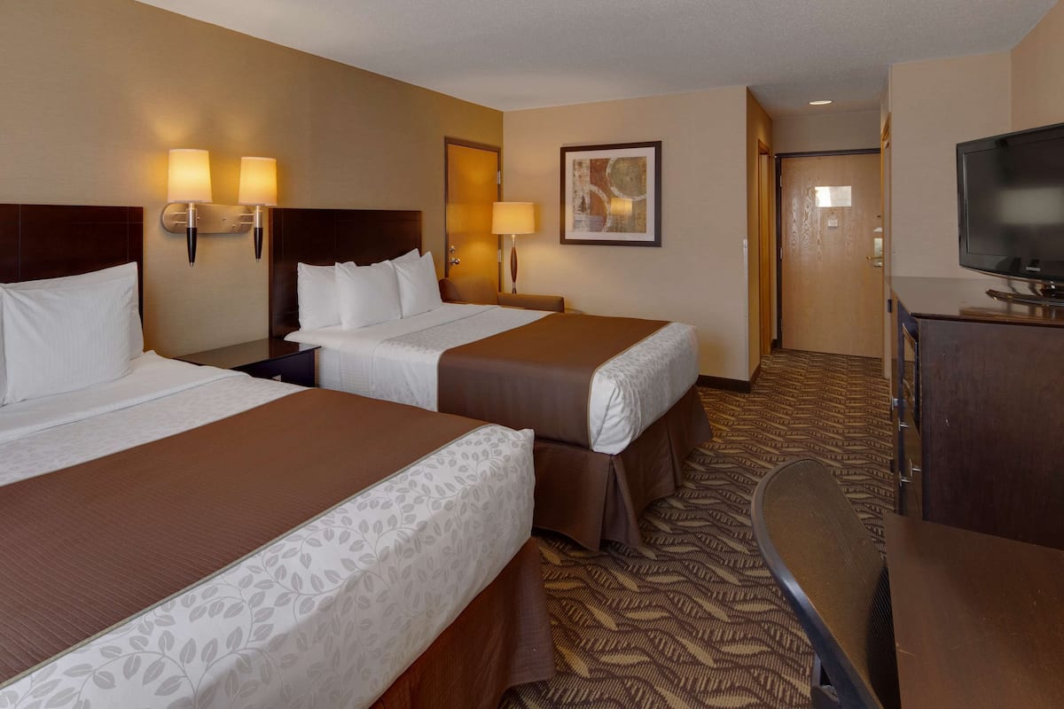 A hotel room with two beds, a desk, a television, and a door leading to another room.