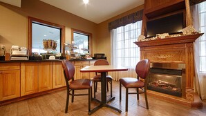 A dining area with a wooden table and chairs, a fireplace, and a kitchen counter with a coffee machine and display case. - Best Western Pontiac Inn (Pontiac)