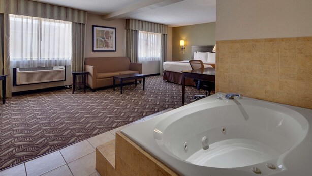 A hotel room with a large bathtub, a sofa, a coffee table, and a desk. - Best Western Pontiac Inn (Pontiac)