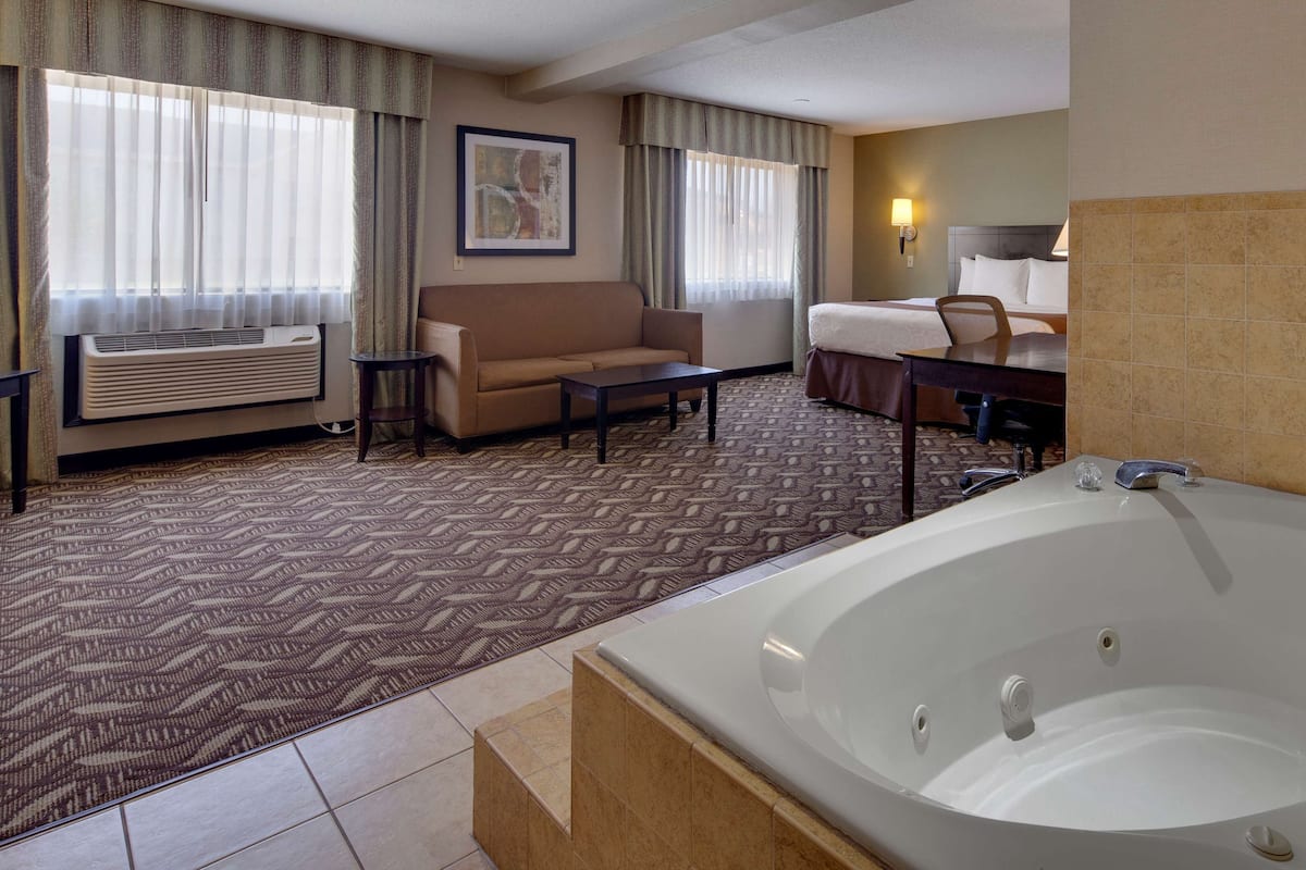 A hotel room with a large bathtub, a sofa, a coffee table, and a desk.