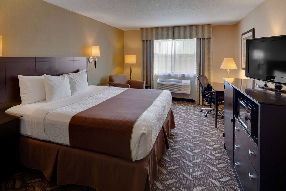 A hotel room with a large bed, two bedside lamps, a TV, a desk, and a chair.