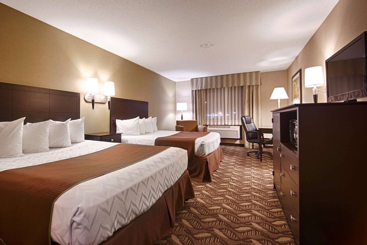 A hotel room with two beds, a desk, a chair, a television, and a wardrobe.