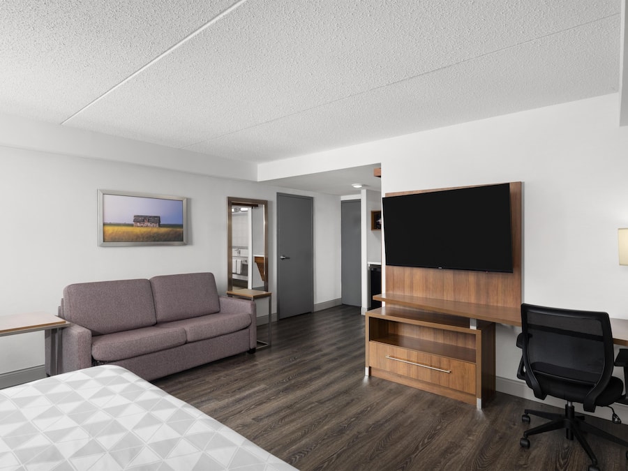 A hotel room with a bed, a sofa, a desk with a flat-screen TV, a chair, and a wooden cabinet.
