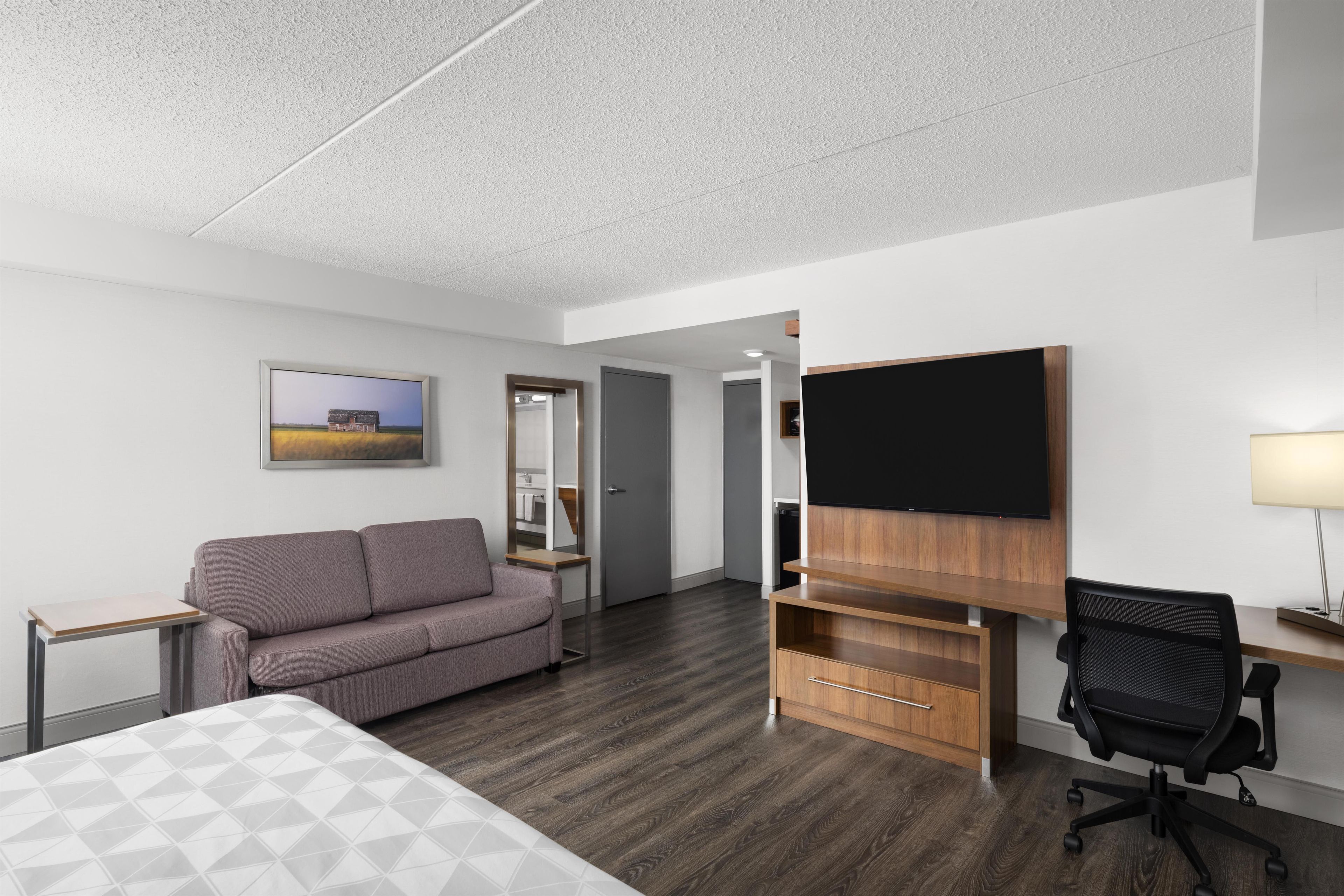 Une chambre d’hôtel comprenant un lit, un canapé, un bureau avec un téléviseur à écran plat, une chaise et une armoire en bois.