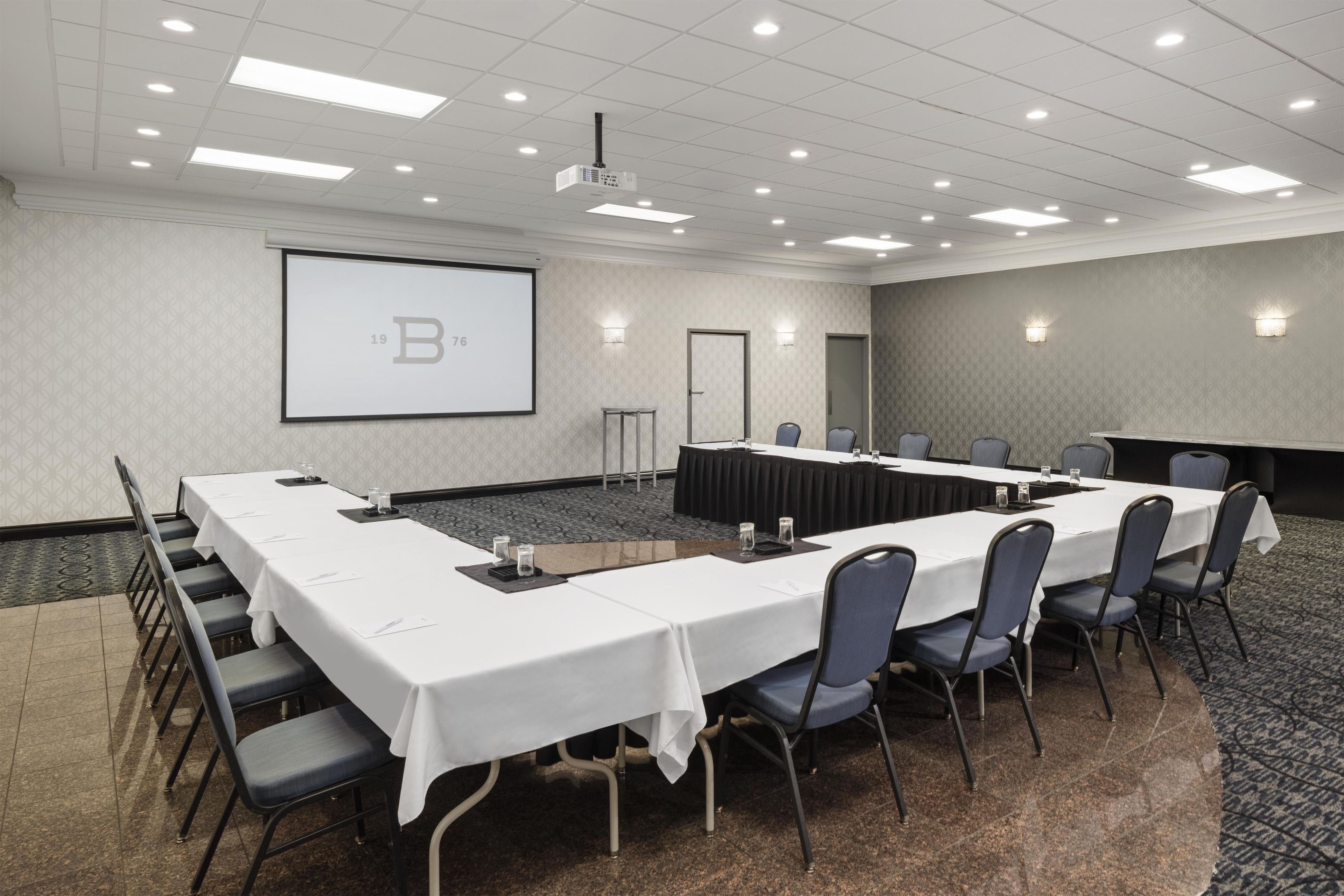 A conference room with a long table, chairs, a projector screen, and a carpeted floor.