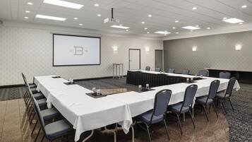 A conference room with a long table, chairs, a projector screen, and a carpeted floor.