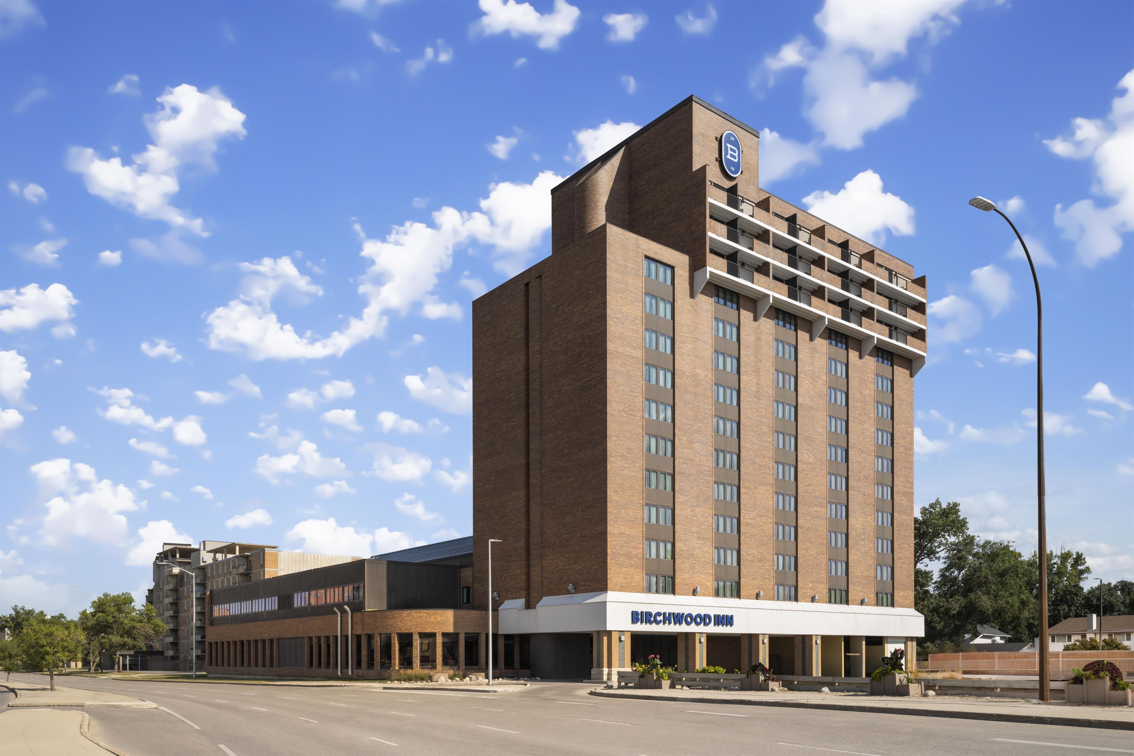A multi-story hotel with a prominent 'BIRCHWOOD INN' sign, featuring a modern brick facade and a flat roof.