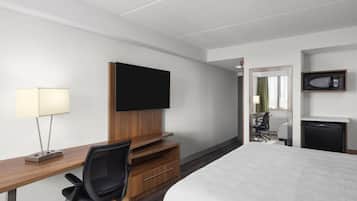 A hotel room with a bed, a desk with a chair, a television, a microwave, and a small refrigerator.