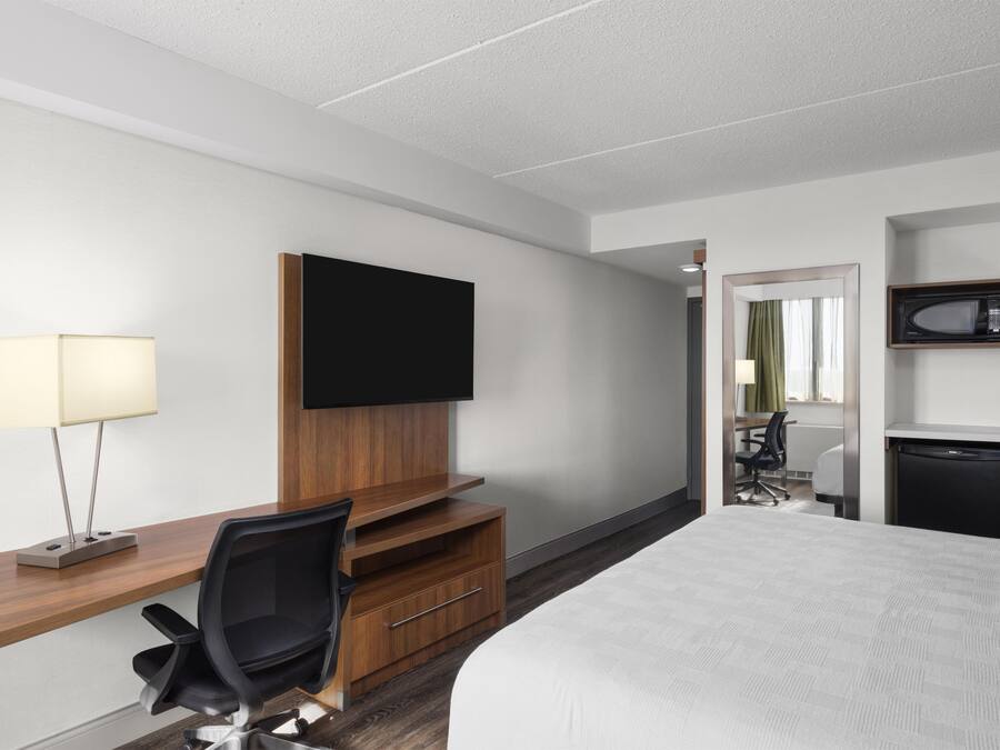 A hotel room with a bed, a desk with a chair, a television, a microwave, and a small refrigerator.