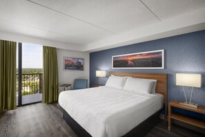 A hotel room with a large bed, two bedside lamps, a nightstand, a chair, a window with curtains, and a cityscape painting on the wall. - Birchwood Inn, BW Premier Collection (Winnipeg)