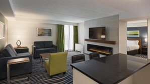 Una habitación de hotel moderna con sofá, sillones, mesa de comedor, televisor de pantalla plana, chimenea y cama.