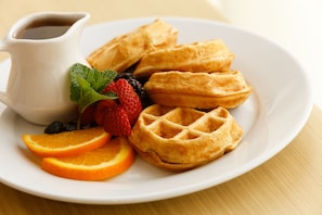 Un plato con waffles, fresas, arándanos y rodajas de naranja, acompañado de una pequeña jarra de jarabe.