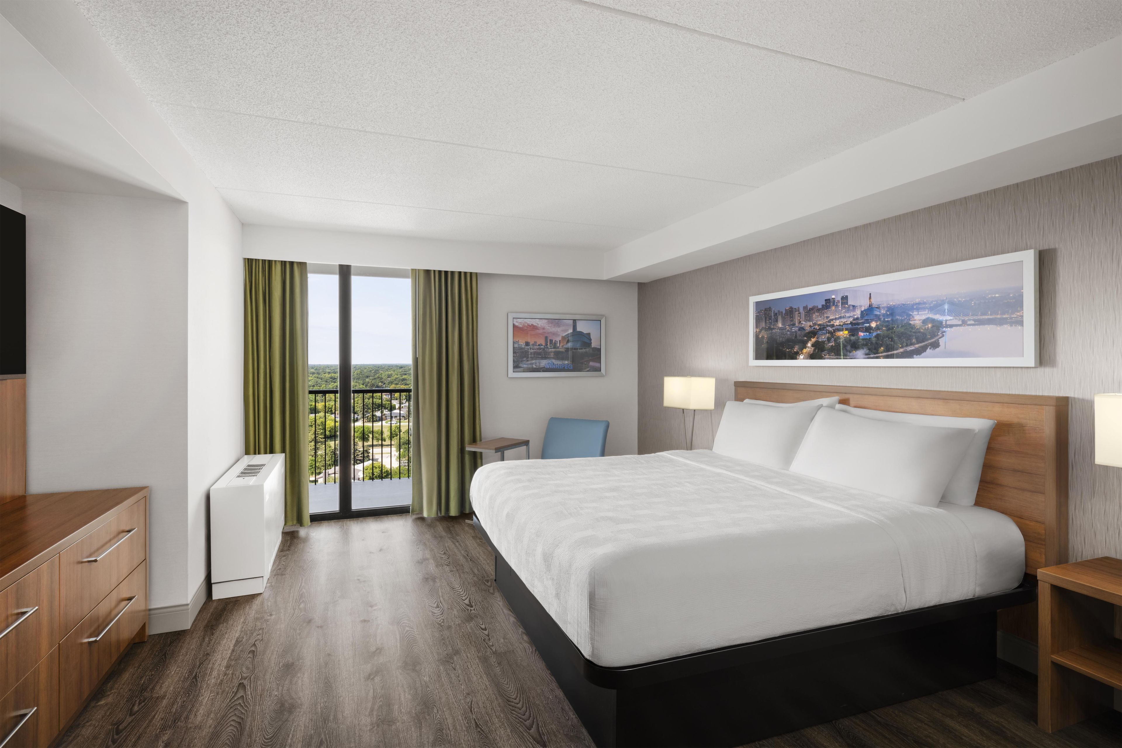 Quarto de hotel com cama, escrivaninha, cadeira, televisão e janela com cortinas.