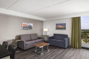 A hotel room with a grey sofa, a smaller grey sofa, a wooden coffee table, a lamp, and two framed pictures on the walls. - Birchwood Inn, BW Premier Collection (Winnipeg)