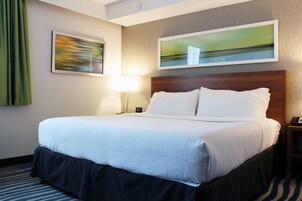 Habitación de hotel con una cama grande, cabecera, lámpara y dos cuadros en la pared.