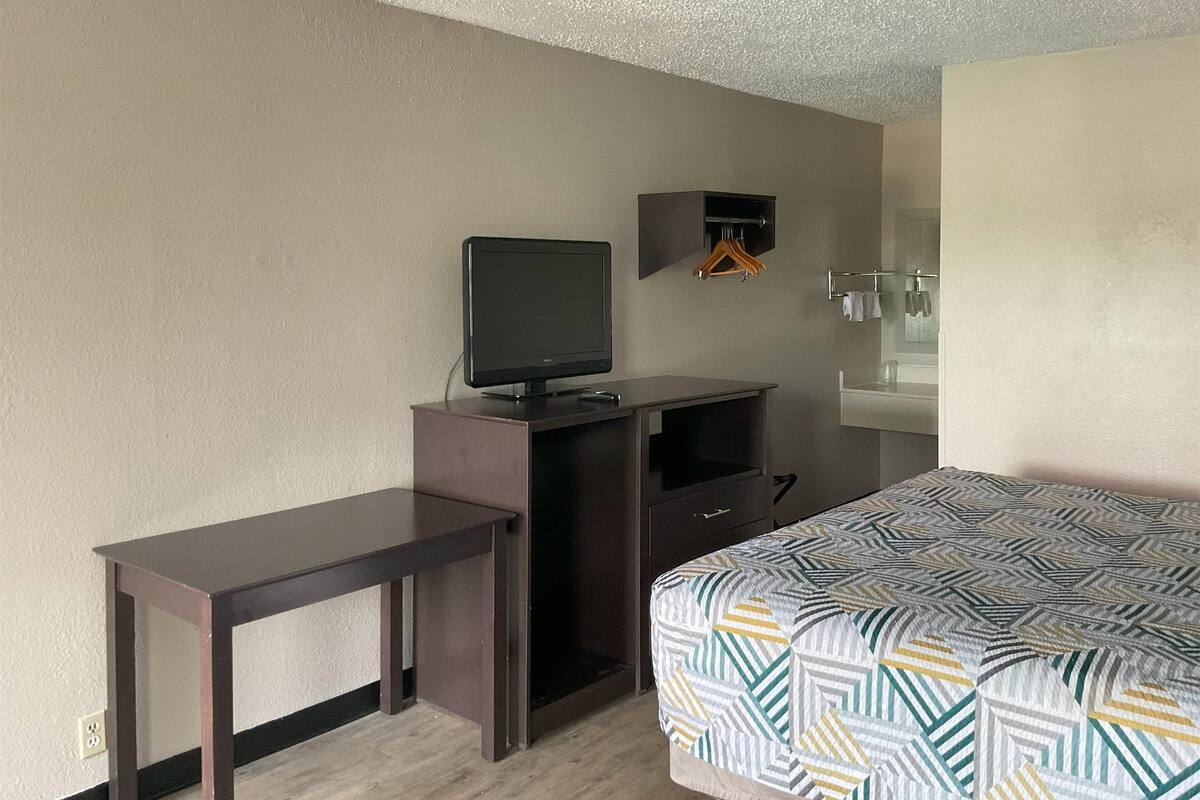 A hotel room with a bed, a desk, a television, a mirror, and a small shelf.