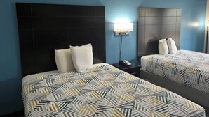 A hotel room with two beds, each with a patterned bedspread, a dark headboard, and a bedside table with a lamp.