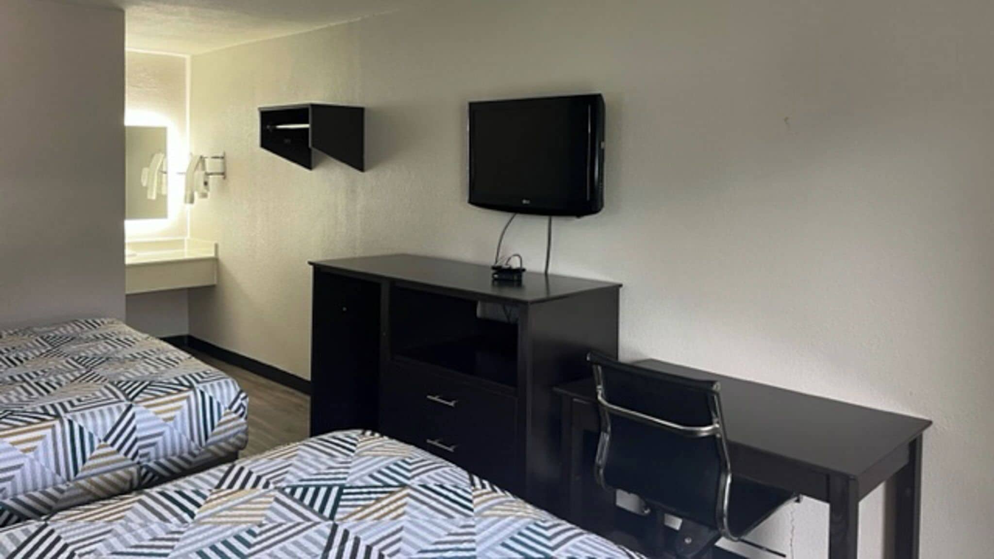 A room with two beds, a desk, a chair, a flat-screen TV, and a window.