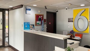 A reception desk with a large number '6' sign, a calendar, and a security camera.