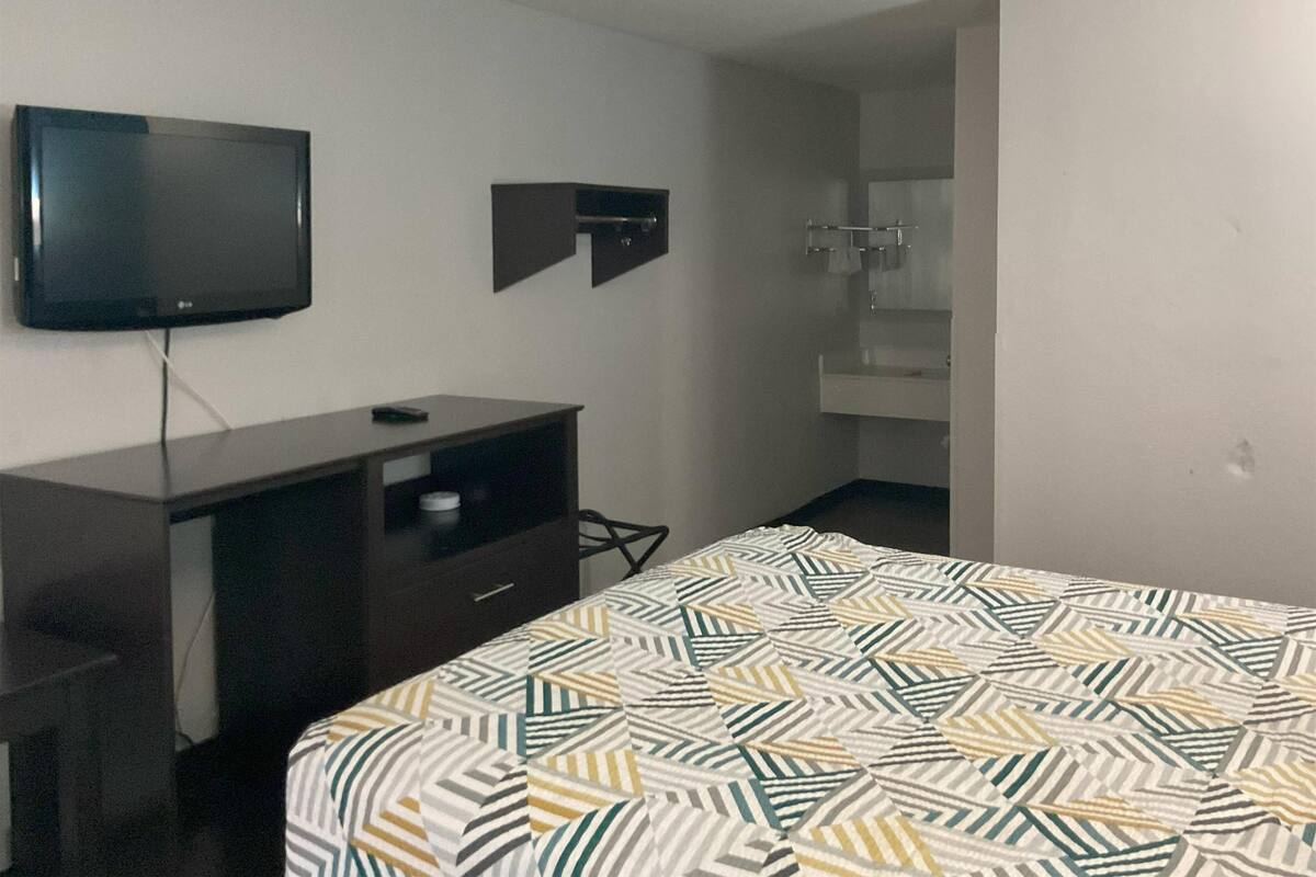 A hotel room with a bed, a TV mounted on the wall, a small desk, and a wardrobe.