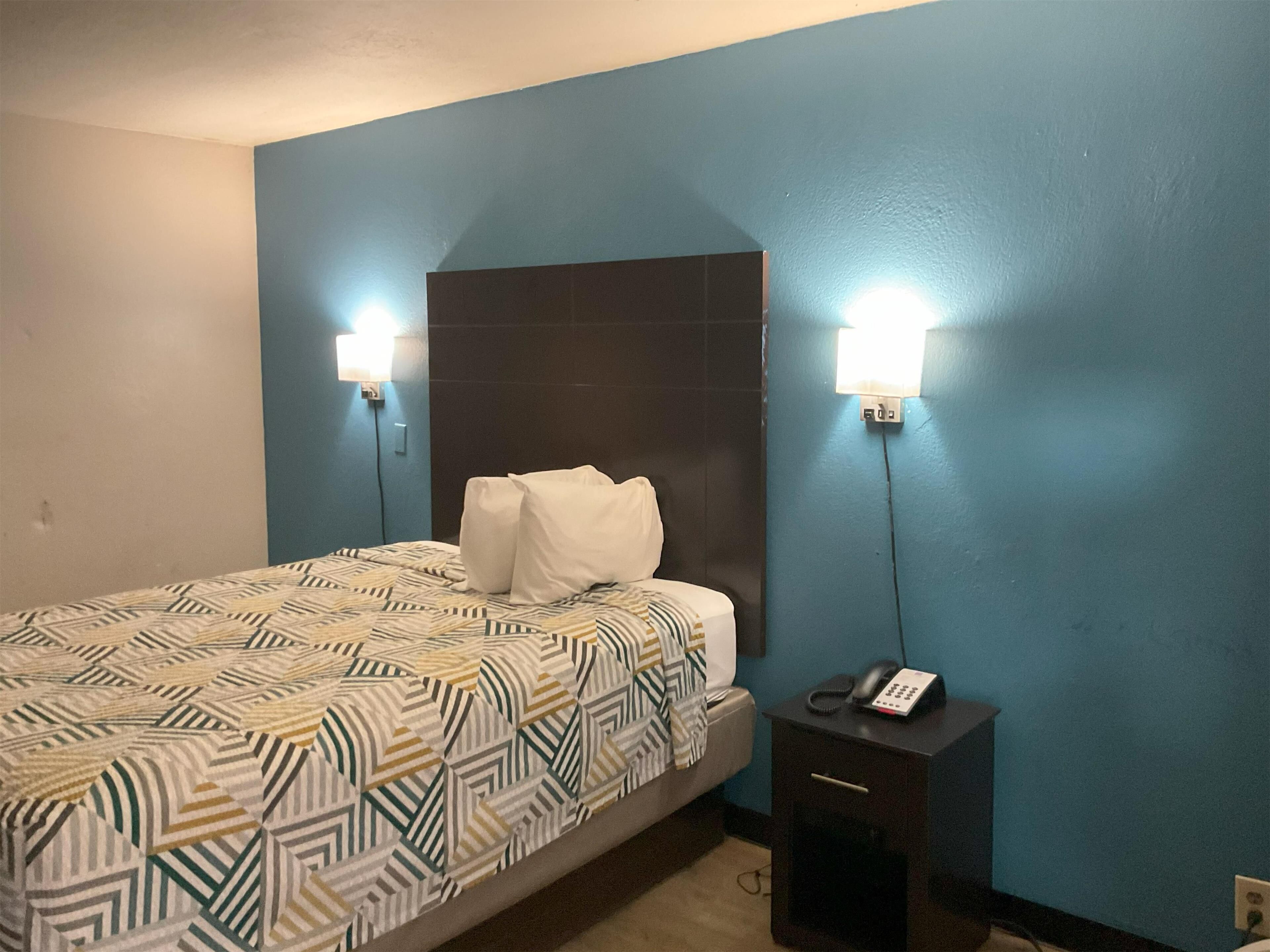 A hotel room with a bed, a nightstand, and two wall-mounted lights.